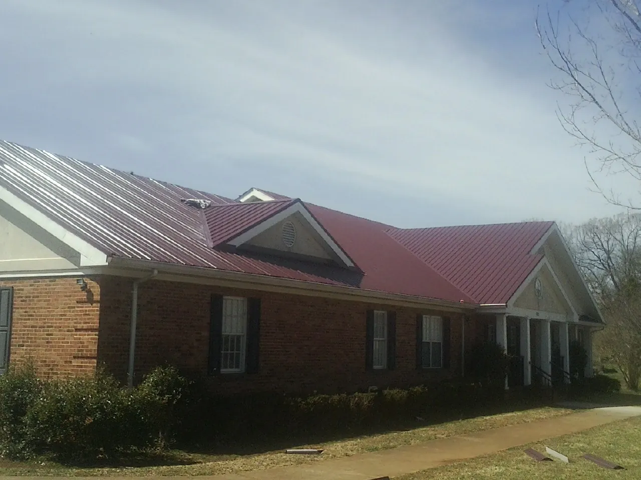 Red metal roof with gabled entries on a long brick building, from a Hail Damage Roof Repair job in Brewster